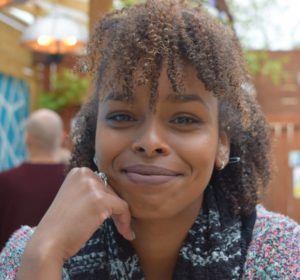 Ayan, our bookings coordinator smiles warmly toward the camera. She rests her face on her right hand.