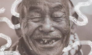 An elderly man with eyes closed and smiling to reveal a few teeth